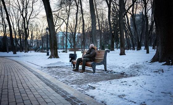 Una persona descansa en un banco de un parque ucraniano nevado durante el crepúsculo.